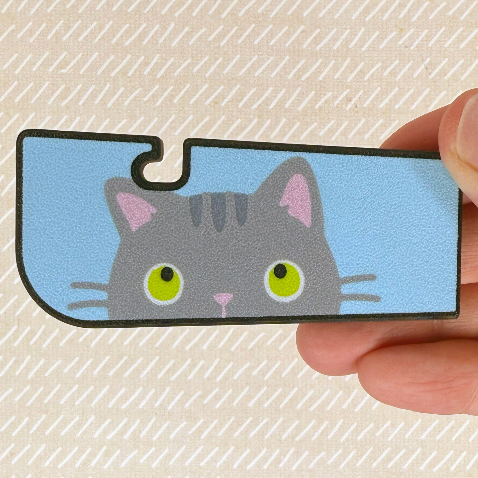 Tab Buddy XL with grey cat design held by a hand on a textured beige background