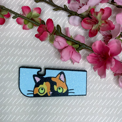 A Tab Buddy XL in Sneaky Tortoiseshell Cat color variation rests atop a beige surface with cherry blossom flowers in background.