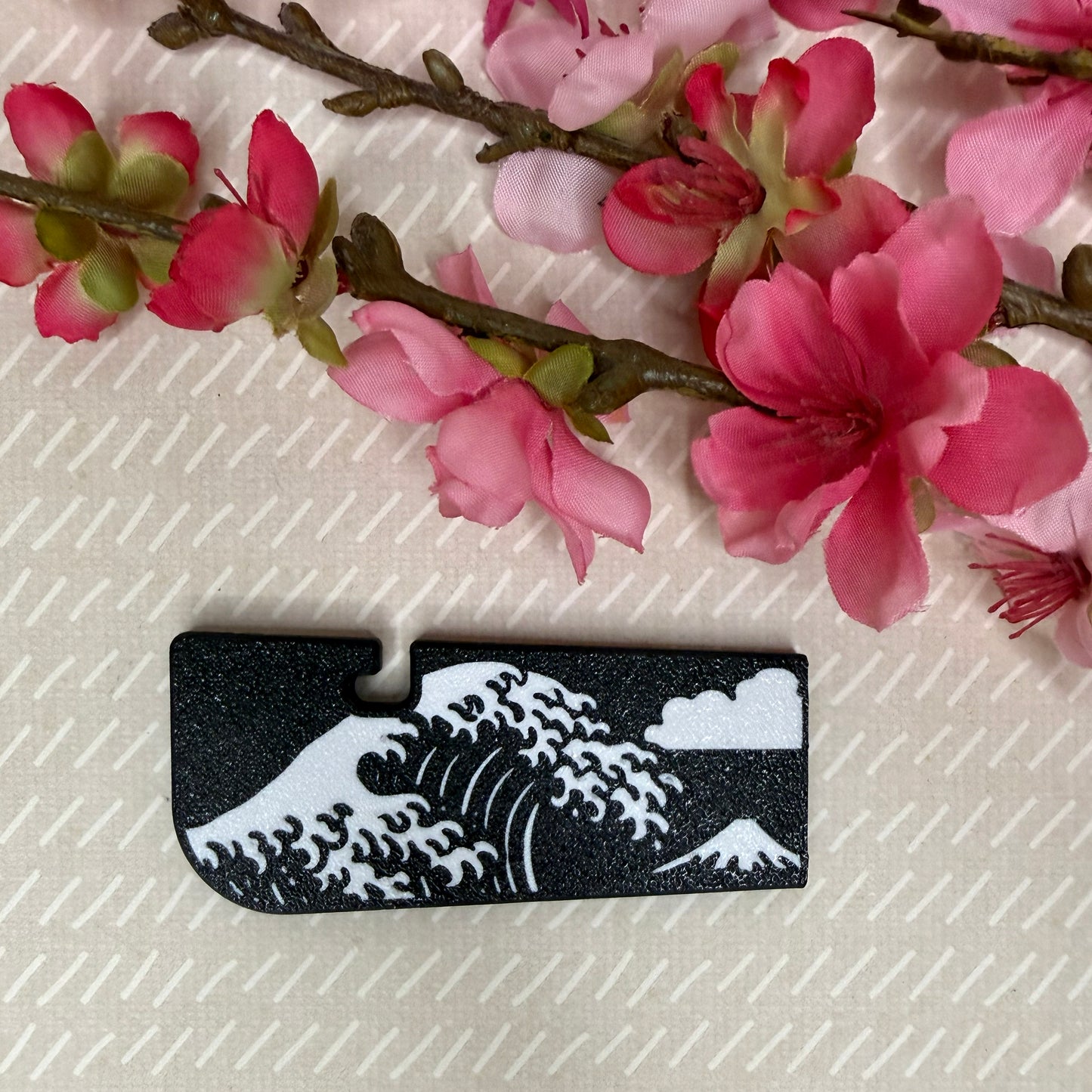A Tab Buddy XL in Great Wave design variation rests atop a beige surface with cherry blossom flowers in background.