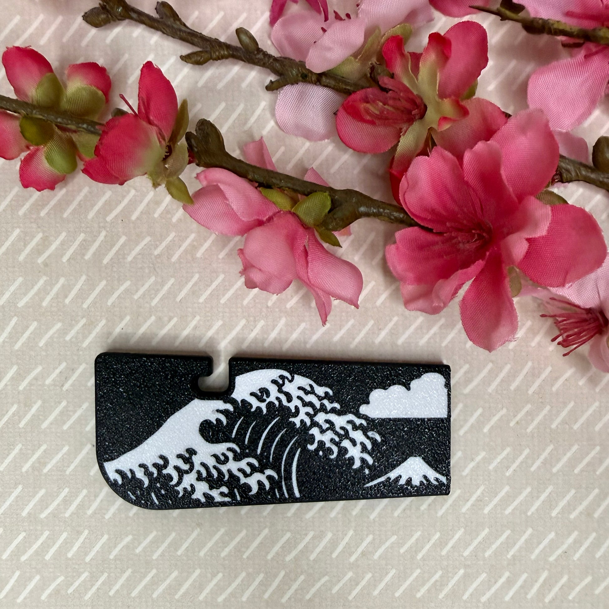 A Tab Buddy XL in Great Wave design variation rests atop a beige surface with cherry blossom flowers in background.