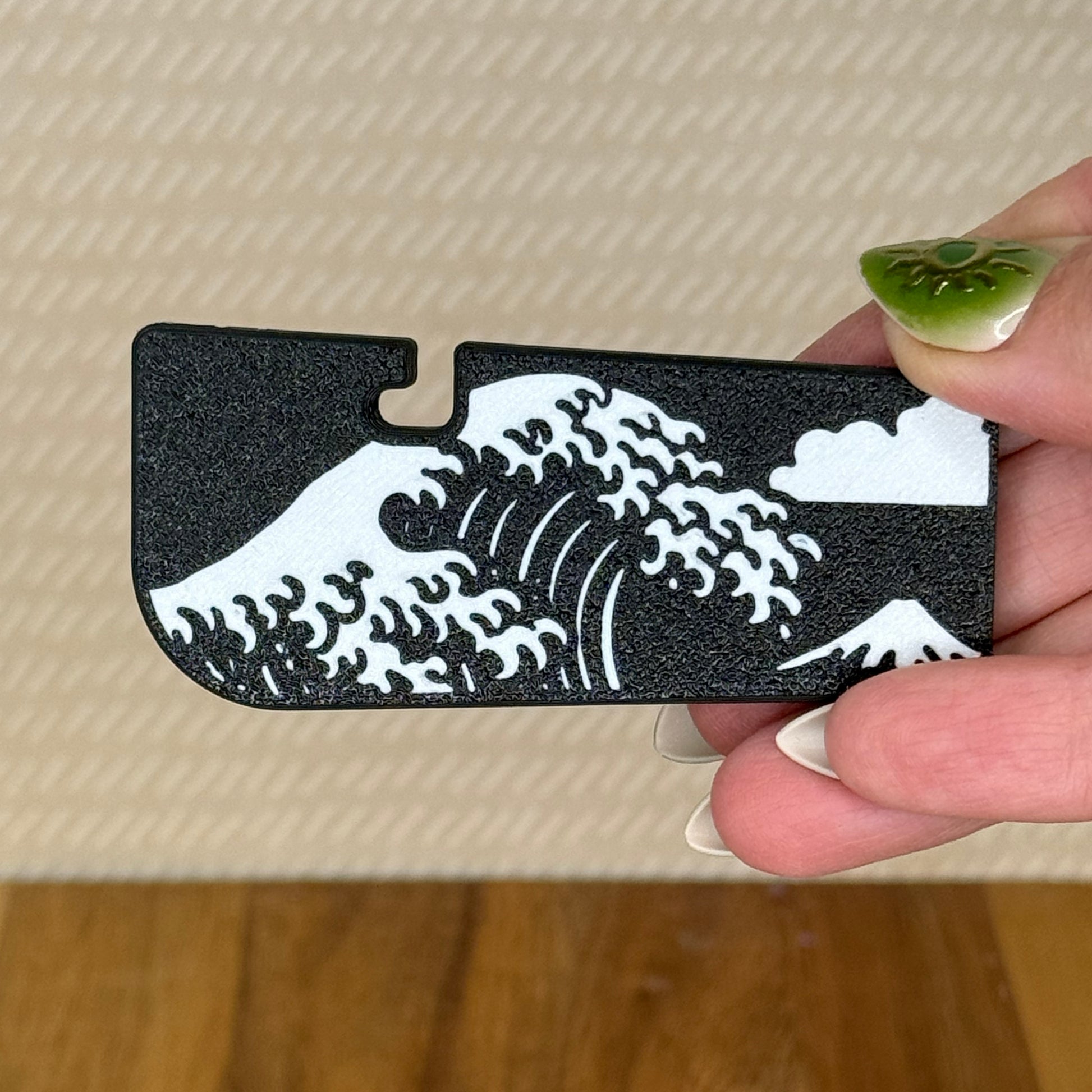 A Tab Buddy XL with a black and white Great Wave off Kanagawa design is held in a hand against a beige background. 