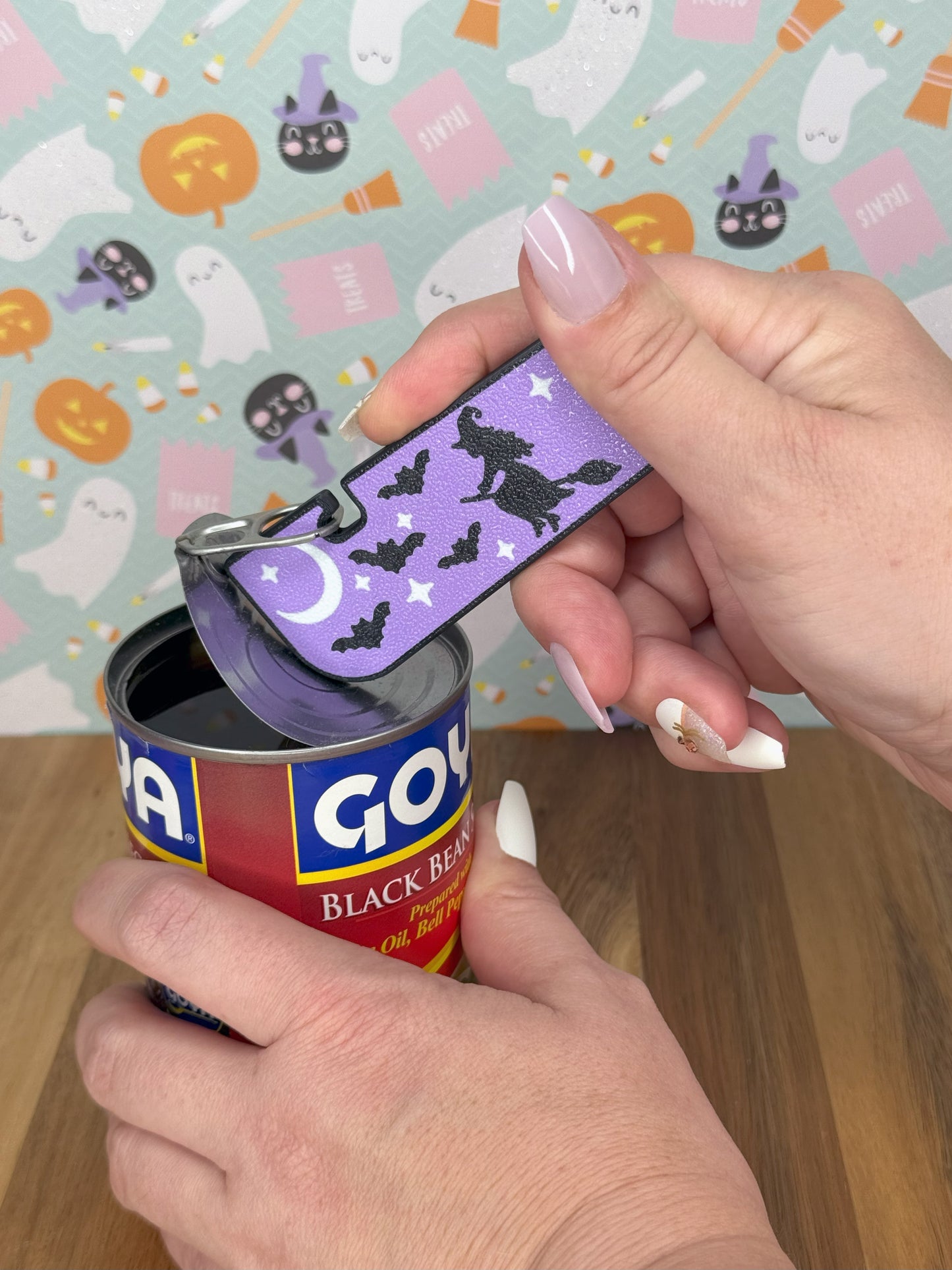 Tab Buddy XL with a decorative purple witch and bat designs on a Halloween-themed background opening a can.