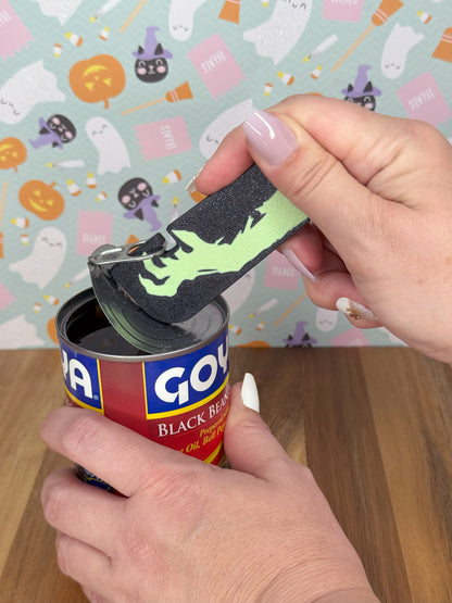 Tab Buddy XL with hand design opening a can of black beans with Halloween-themed wallpaper in the background