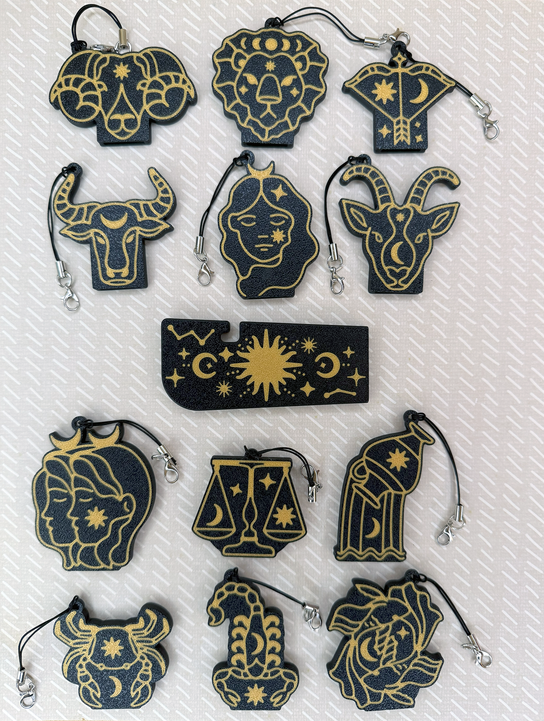 Collection of zodiac-themed Tab Buddies keychains on a textured white and beige background