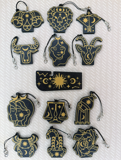 Collection of zodiac-themed Tab Buddies keychains on a textured white and beige background